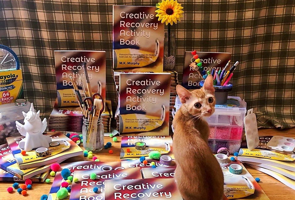 An orange cat on copies of the Creative Recovery Activity Book
